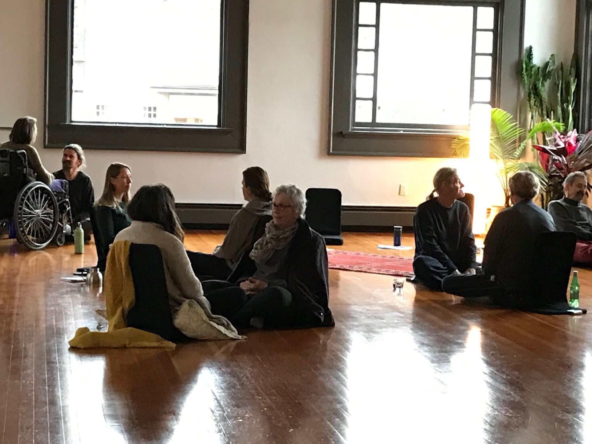 groups of people sitting together on wood floor, sun through windows 